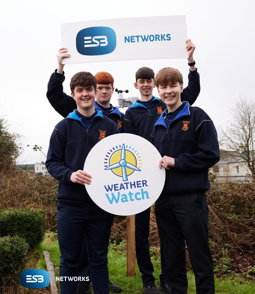 Four students standing outdoors with a weather station, holding banners featuring the ESB Networks logo and Weather Watch logo.